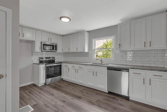 kitchen with stainless steel appliances, a sink, light stone counters, and white cabinets