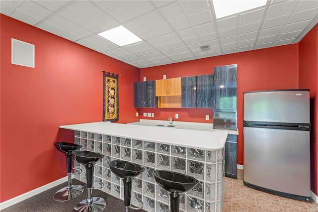 kitchen with freestanding refrigerator, a breakfast bar, and baseboards