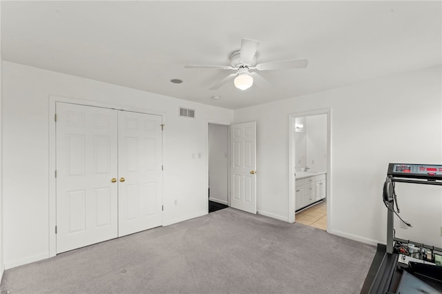 unfurnished bedroom with light colored carpet, a closet, baseboards, a ceiling fan, and connected bathroom