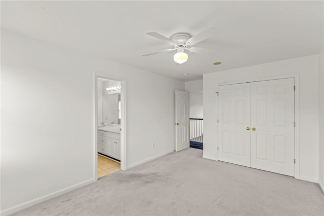 unfurnished bedroom featuring light carpet, a closet, baseboards, ensuite bath, and ceiling fan