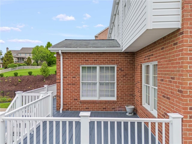 view of home's exterior featuring brick siding, a deck, and roof with shingles