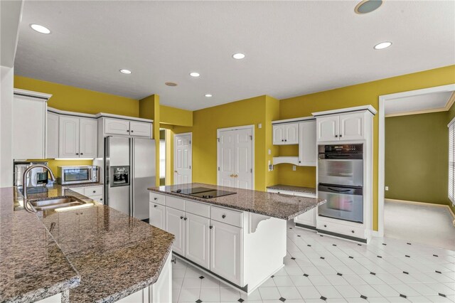 kitchen featuring stainless steel appliances, a sink, a center island, white cabinetry, and recessed lighting