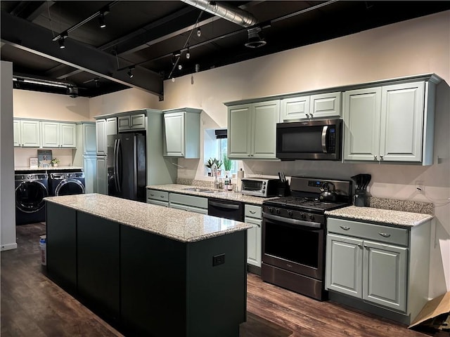kitchen with black appliances, washing machine and clothes dryer, dark wood-style flooring, a center island, and track lighting