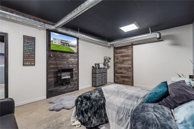 bedroom with a barn door, concrete floors, baseboards, and a glass covered fireplace