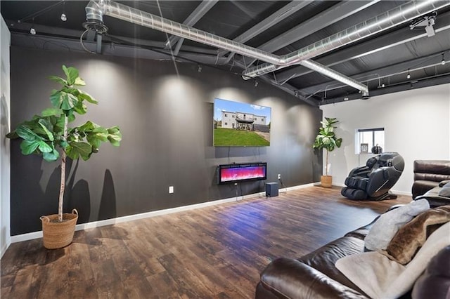 home theater room featuring wood finished floors, baseboards, track lighting, and a glass covered fireplace