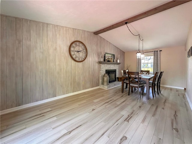 dining space featuring wood finished floors, wooden walls, a stone fireplace, and baseboards