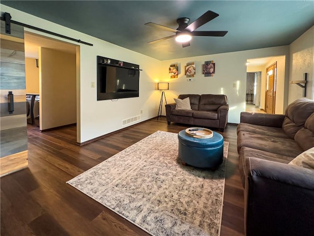 living area with a barn door, a ceiling fan, and dark wood finished floors