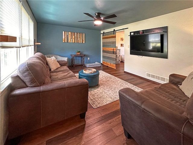 living room with ceiling fan, a barn door, wood finished floors, and baseboards