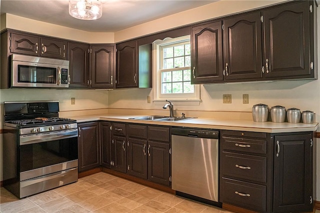 kitchen featuring appliances with stainless steel finishes, a sink, light countertops, and dark brown cabinets
