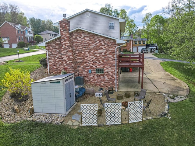 back of house with brick siding, a lawn, a patio area, a chimney, and a wooden deck