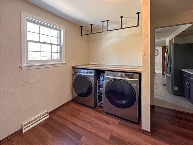 laundry room featuring washing machine and dryer, wood finished floors, a textured wall, and baseboards