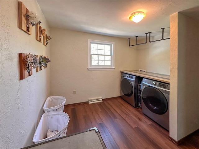 clothes washing area featuring washing machine and dryer, wood finished floors, a textured wall, and baseboards