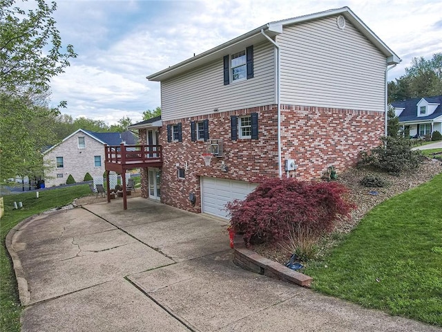 view of home's exterior with driveway, brick siding, a garage, a wooden deck, and a lawn