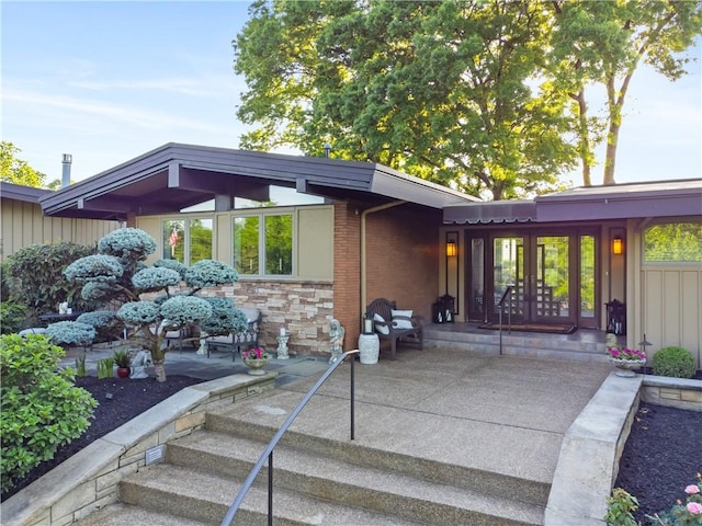 view of exterior entry with french doors, board and batten siding, a patio, and stone siding