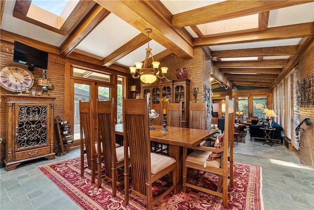 dining room featuring stone tile floors, a chandelier, a skylight, and wooden walls