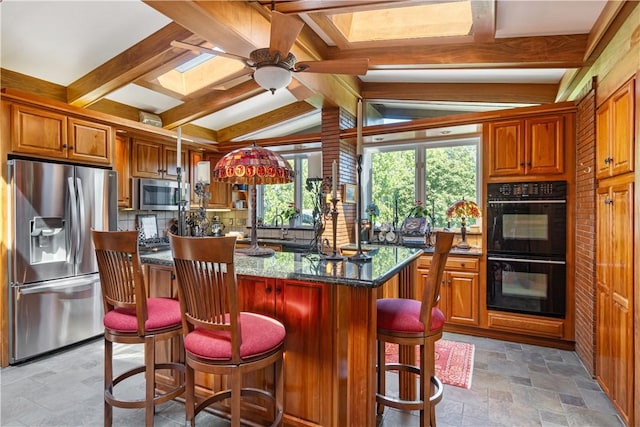 kitchen featuring appliances with stainless steel finishes, stone tile flooring, a kitchen island, a ceiling fan, and a breakfast bar area