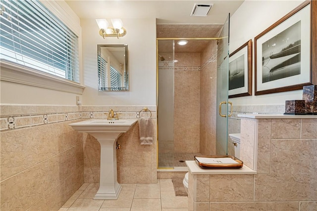bathroom with tile patterned floors, tile walls, a shower stall, a wainscoted wall, and a sink