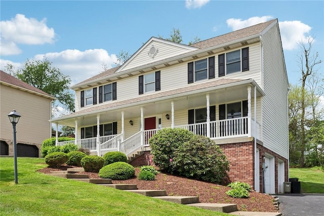 view of front of home featuring an attached garage, brick siding, a porch, driveway, and a front yard