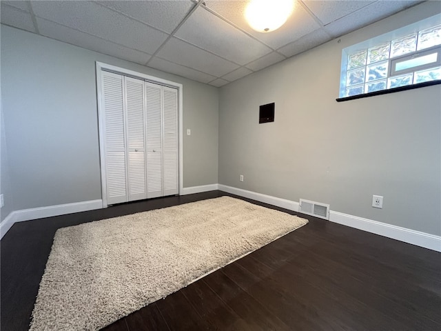 unfurnished bedroom featuring a drop ceiling, dark wood finished floors, baseboards, and a closet