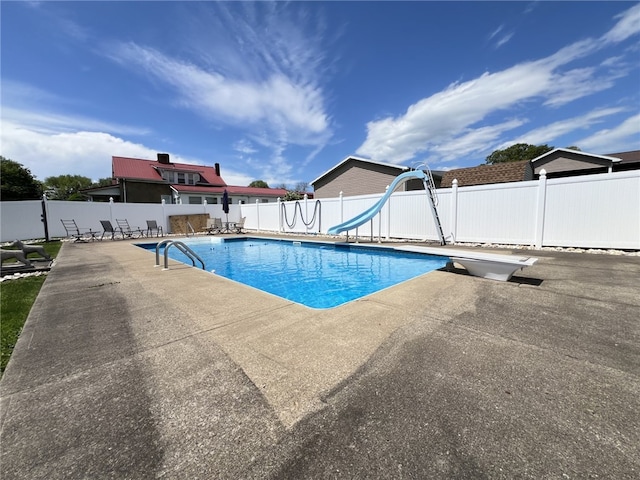 view of pool with a patio area, fence, a water slide, and a diving board