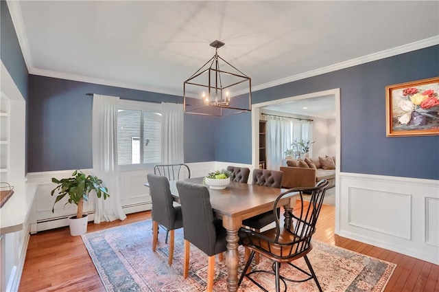dining room with a wainscoted wall, a chandelier, a decorative wall, light wood-type flooring, and ornamental molding