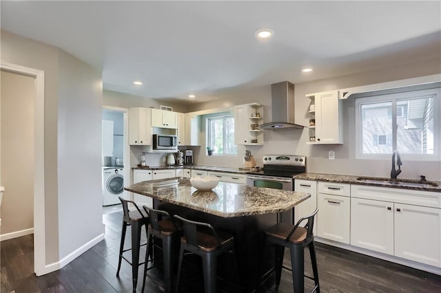 kitchen with wall chimney exhaust hood, stainless steel appliances, washer / dryer, a sink, and open shelves