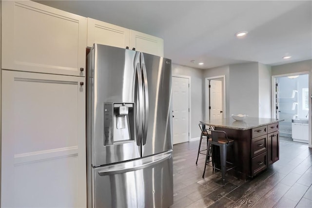 kitchen with stainless steel refrigerator with ice dispenser, light stone countertops, dark wood-style flooring, a center island, and a kitchen bar
