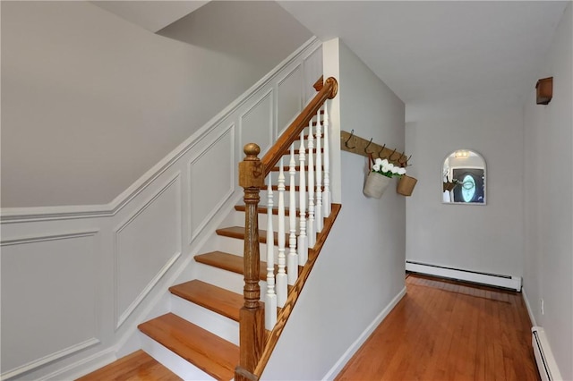 stairway with a baseboard radiator, a decorative wall, wood finished floors, and baseboards