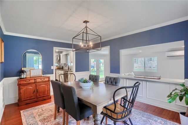dining space with a wall mounted AC, a decorative wall, wood finished floors, a chandelier, and a wainscoted wall