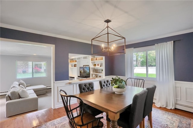 dining area with wood finished floors, a chandelier, wainscoting, ornamental molding, and a decorative wall