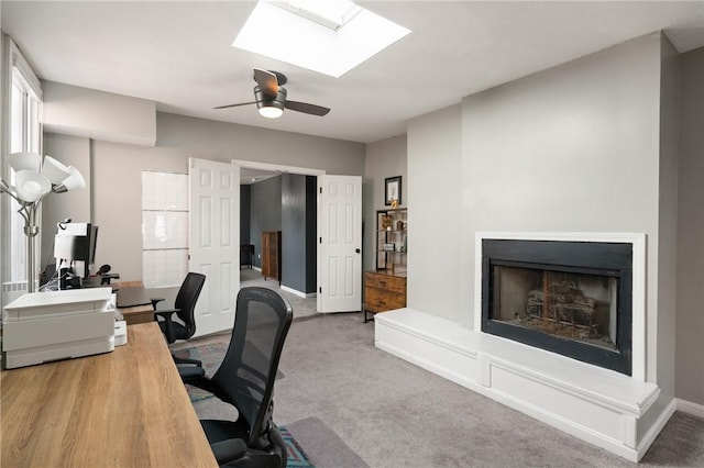office space with a fireplace with raised hearth, a skylight, carpet, a ceiling fan, and baseboards