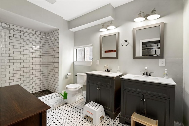 full bath with tiled shower, two vanities, and toilet