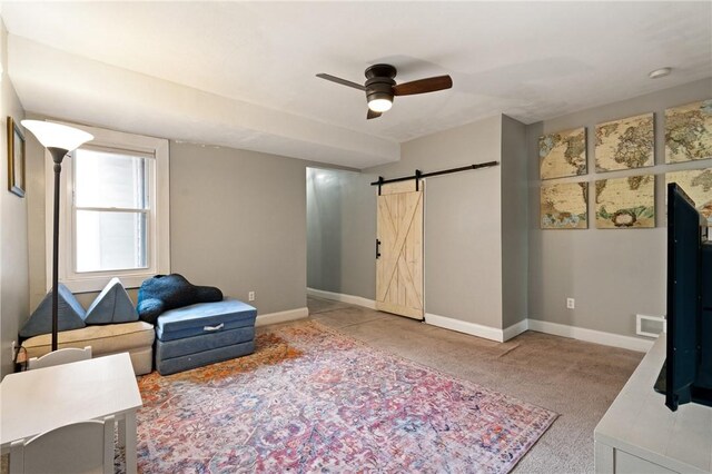 living area with carpet floors, a barn door, ceiling fan, and baseboards