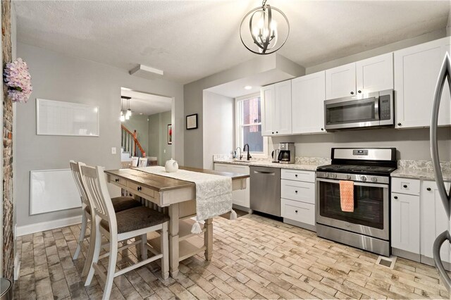 kitchen with appliances with stainless steel finishes, a sink, a chandelier, and brick patterned floors