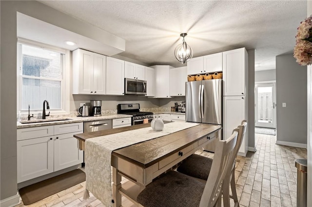 kitchen featuring appliances with stainless steel finishes, a sink, white cabinets, decorative light fixtures, and a textured ceiling
