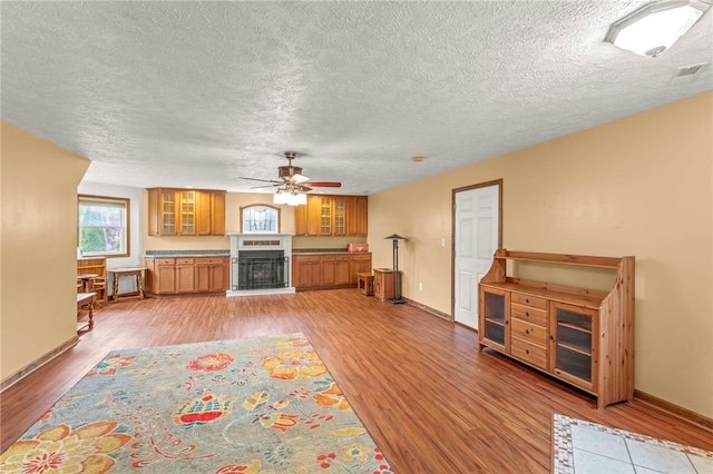 128 Evergreen Dr, Peters Twp, PA 15317 - living room featuring light wood-type flooring, a ceiling fan, a fireplace with raised hearth, a textured ceiling, and baseboards