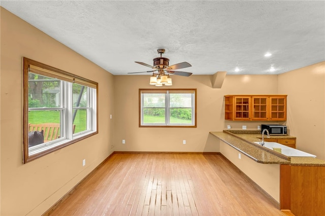 128 Evergreen Dr, Peters Twp, PA 15317 - kitchen featuring stainless steel microwave, brown cabinets, a peninsula, light wood-style flooring, and glass insert cabinets