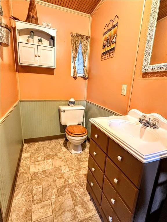 half bath featuring toilet, a wainscoted wall, wood ceiling, vanity, and baseboards