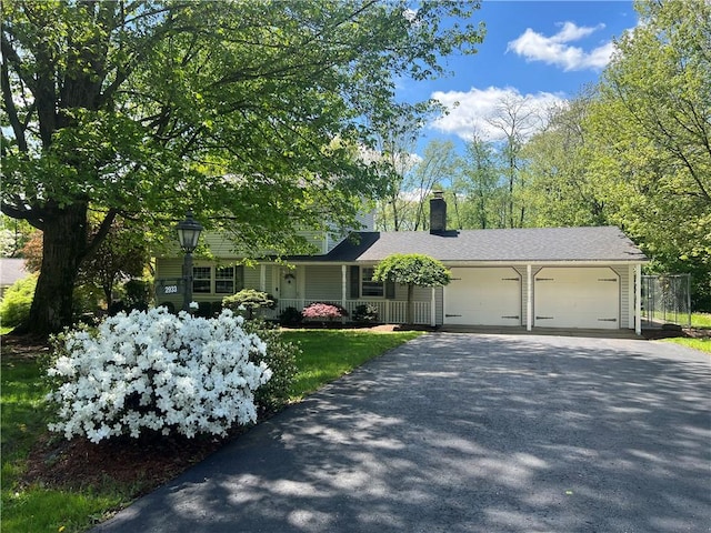 view of front facade with asphalt driveway, a garage, and a chimney