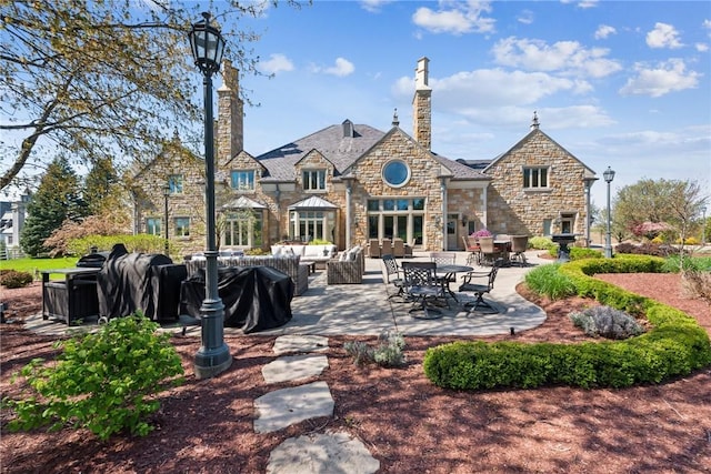back of property with stone siding, outdoor lounge area, a patio, and a chimney