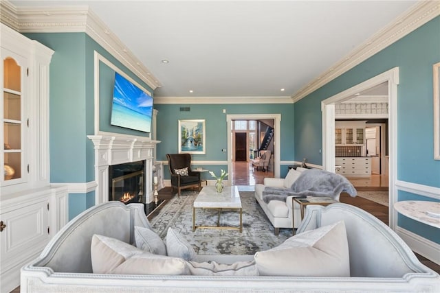 living room featuring wood finished floors, crown molding, a glass covered fireplace, baseboards, and recessed lighting