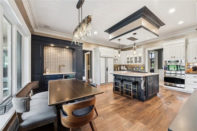 kitchen with stainless steel double oven, tasteful backsplash, white cabinetry, white microwave, and light countertops