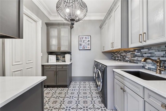 laundry room featuring cabinet space, washer and clothes dryer, crown molding, baseboards, and a chandelier