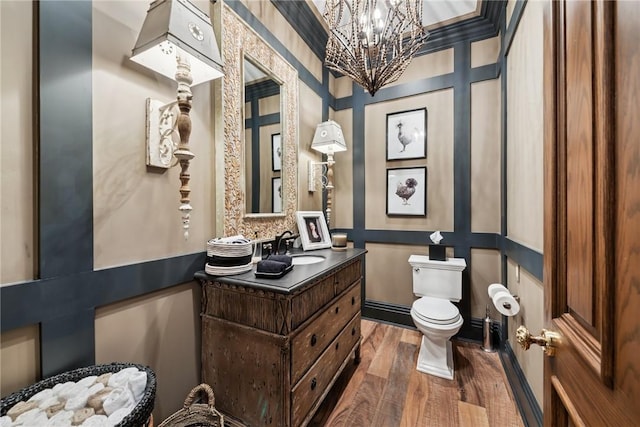 half bath featuring wood finished floors, toilet, a chandelier, and vanity