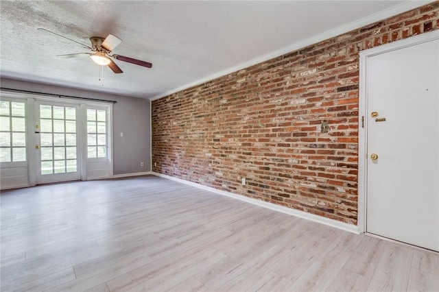 unfurnished room featuring baseboards, brick wall, a ceiling fan, wood finished floors, and a textured ceiling