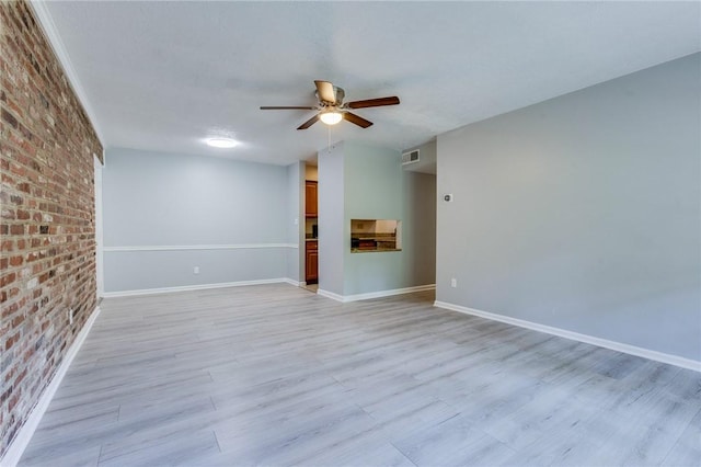 spare room with brick wall, a ceiling fan, light wood finished floors, and baseboards