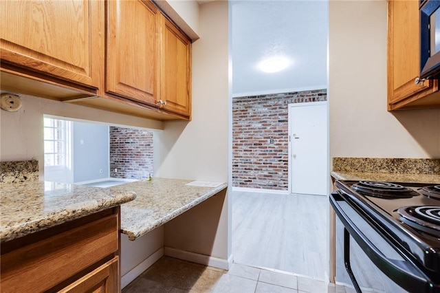 kitchen featuring electric range, brick wall, light stone counters, baseboards, and light tile patterned floors