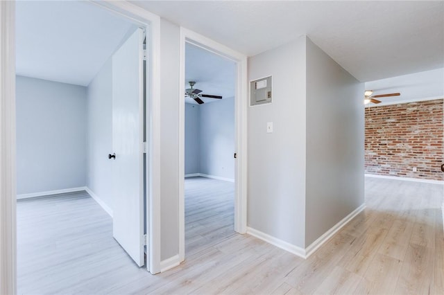 corridor with light wood-style flooring, brick wall, and baseboards