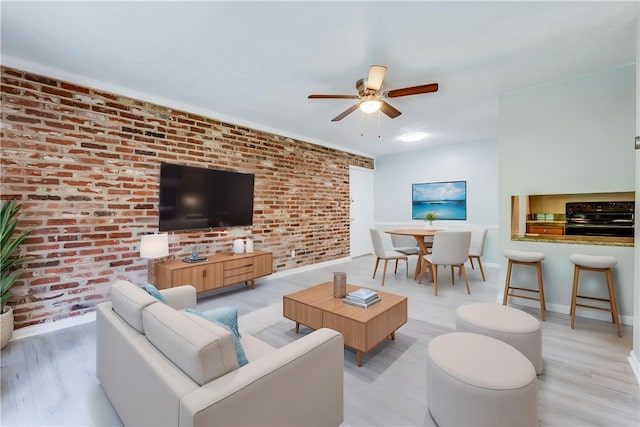 living area featuring brick wall, ceiling fan, baseboards, and wood finished floors