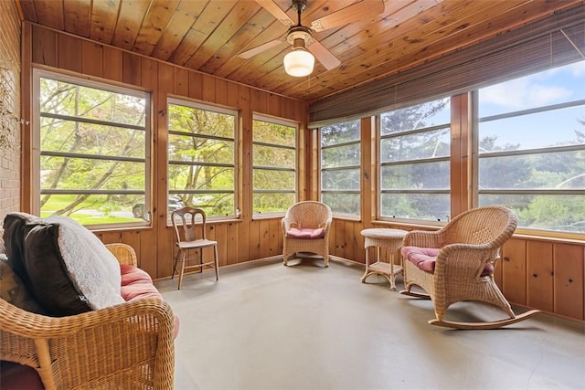 sunroom featuring healthy amount of natural light, a ceiling fan, concrete flooring, and wood walls